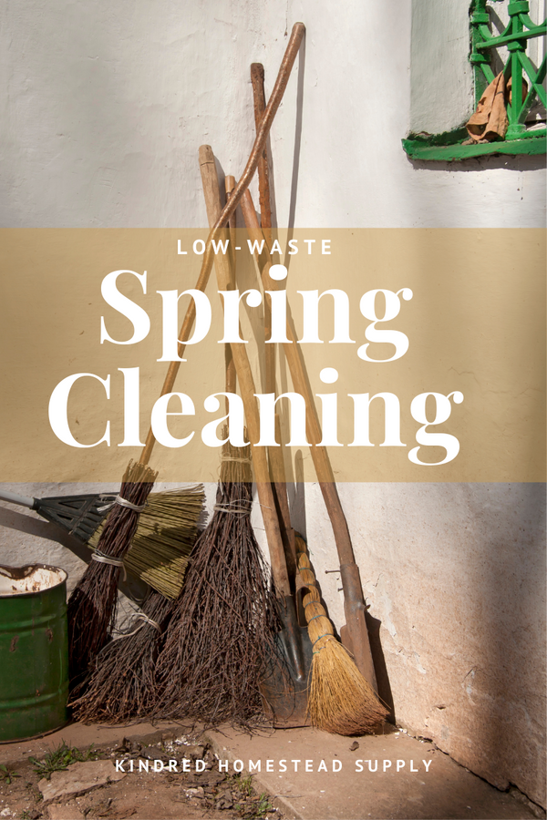 Image of brooms piled in a corner with text over image reading low-waste spring cleaning. Kindred Homestead Supply